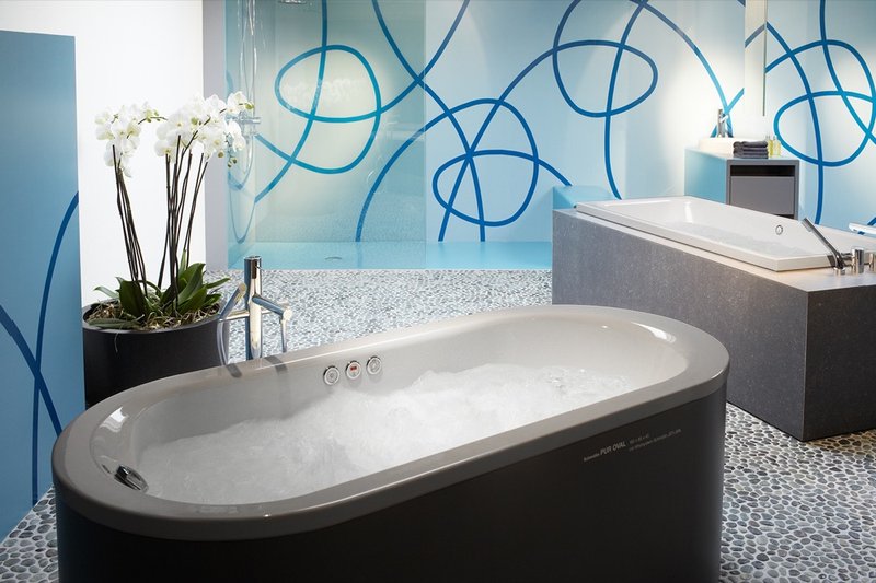 Moderner Ausstellungsbereich mit freistehender Whirlpool-Badewanne und Designbadewanne vor dekorativer blauer Wandgestaltung.