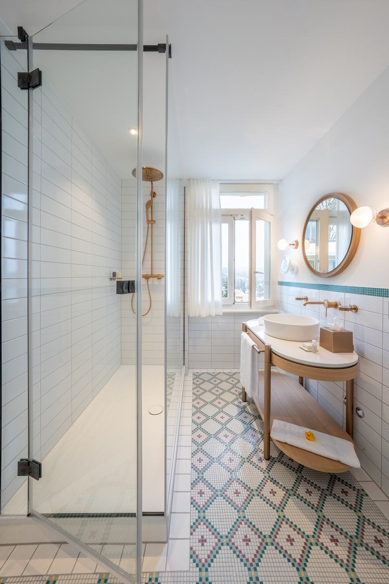 Helles Badezimmer mit begehbarer Dusche, runden Spiegeln und gemustertem Fliesenboden