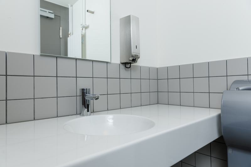 Waschbecken in öffentlichem Sanitärraum mit schlichten Fliesen und minimalistischem Design