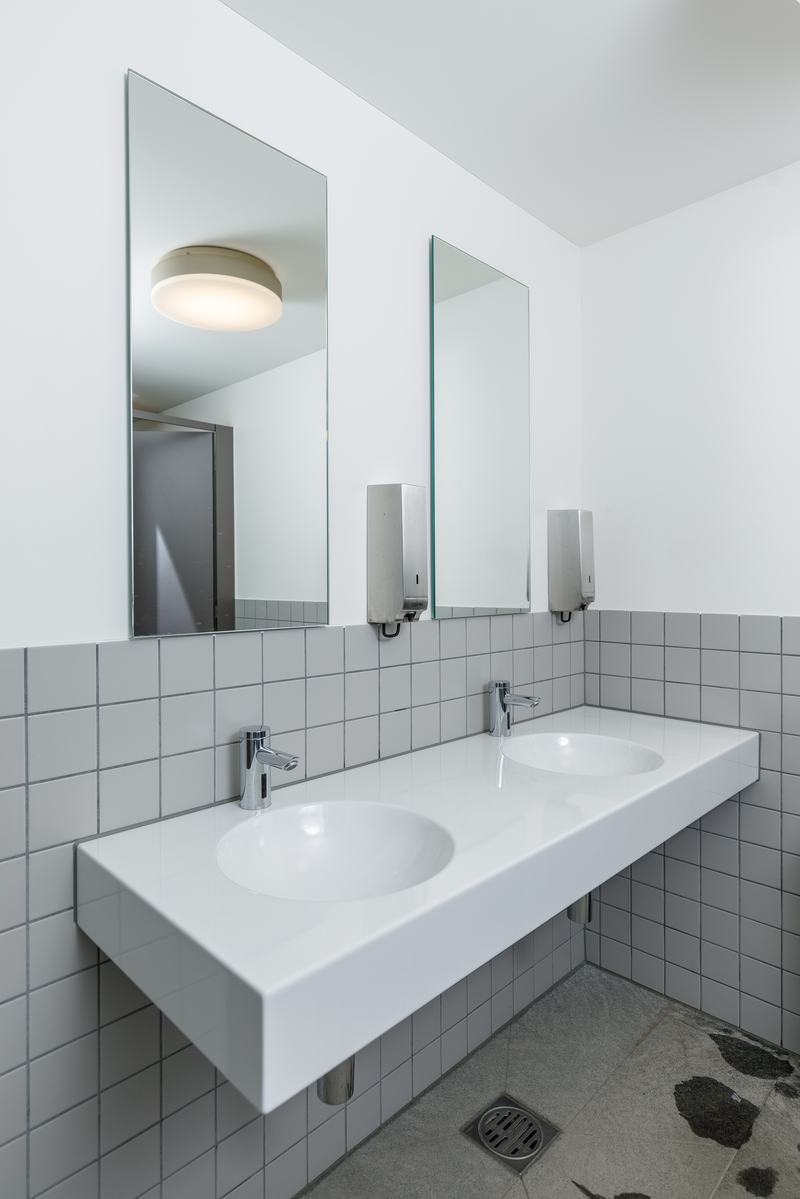 Doppelwaschbecken mit Spiegeln und schlichten Fliesen in modernem Waschraum