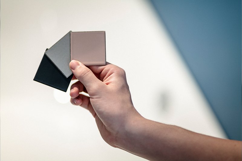 Hand hält drei Materialmuster in verschiedenen Farben vor unscharfem Hintergrund.