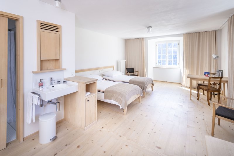 Helles Hotelzimmer mit zwei Einzelbetten, Holzmöbeln und offenem Waschbereich