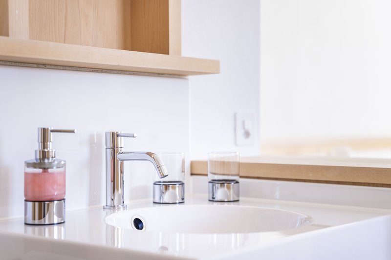 Modernes Waschbecken mit verchromter Armatur und Accessoires in hellem Badezimmer