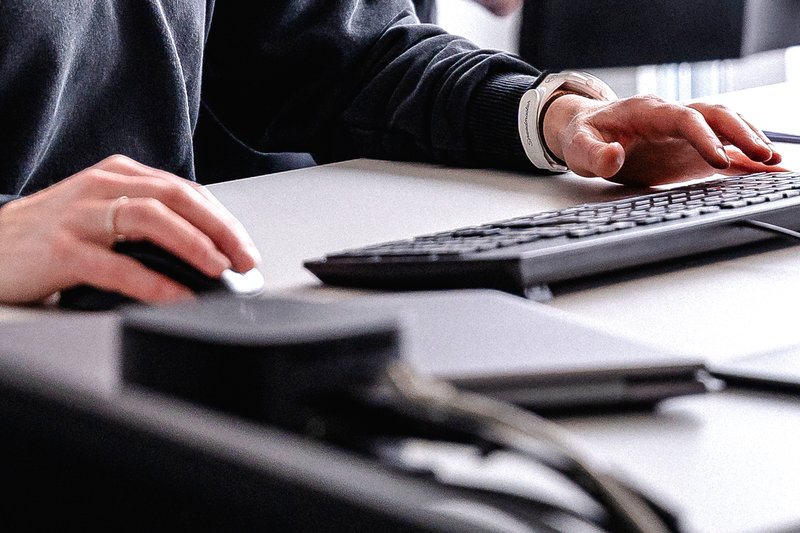 Nahaufnahme von Händen an Tastatur und Maus auf einem Schreibtisch.