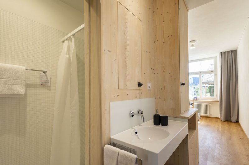 Modernes Badezimmer mit Holzverkleidung, Waschbecken und Blick in ein helles Zimmer
