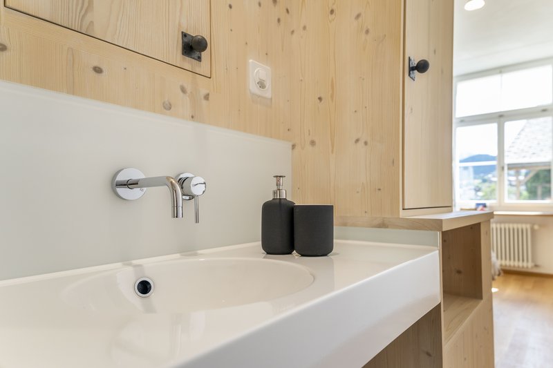 Waschbecken mit Wandarmatur und Holzverkleidung in modernem Badezimmer