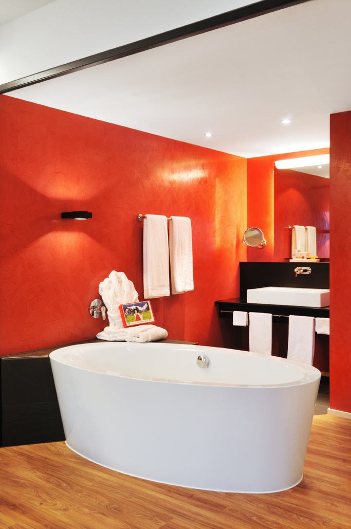 Modernes Badezimmer mit freistehender Badewanne, roten Wänden und schwarzem Waschtisch
