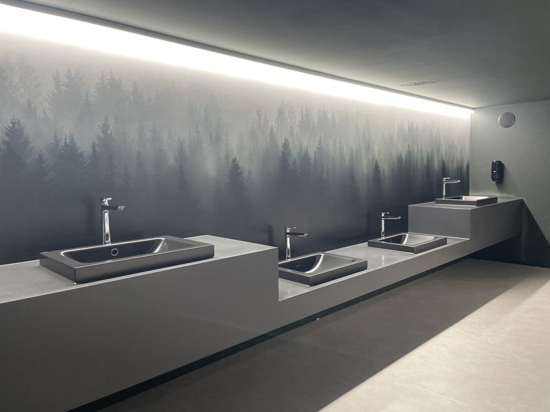 Moderner Waschraum mit mehreren Waschbecken und stimmungsvoller Wandgestaltung mit Waldmotiv