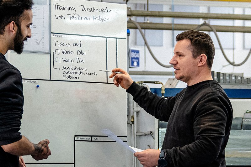 Zwei Mitarbeiter der Wilhelm Schmidlin AG besprechen ein Training vor einem Whiteboard in der Produktion
