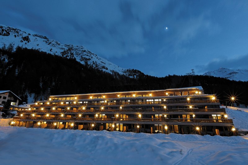 Hotel Nira Alpina in Silvaplana bei Nacht, beleuchtete Fassade vor verschneiter Bergkulisse.