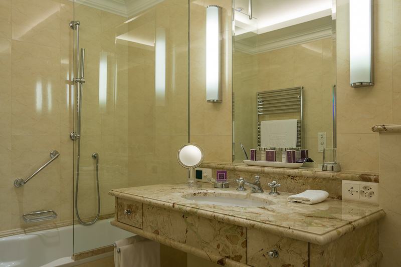 Elegantes Badezimmer mit Marmorwaschtisch, Spiegel, Beleuchtung und Badewanne mit Glasduschwand