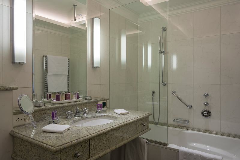 Hochwertiges Badezimmer mit Natursteinwaschtisch, Spiegel, Beleuchtung und Badewanne mit Glasduschwand