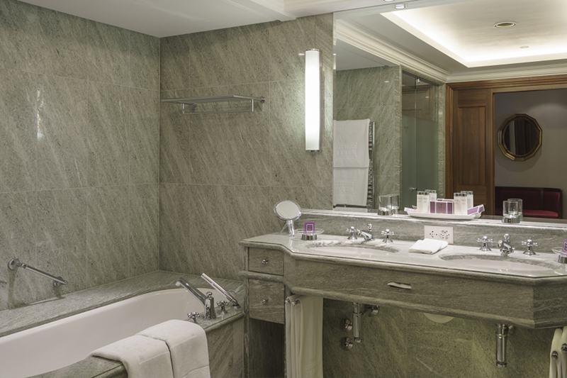 Elegantes Badezimmer mit Natursteinverkleidung, Doppelwaschtisch, Spiegel und Badewanne
