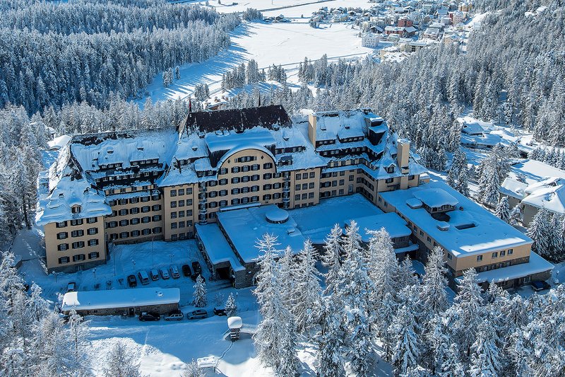 Luftaufnahme des Suvretta House in St. Moritz, umgeben von verschneiter Landschaft und Wäldern
