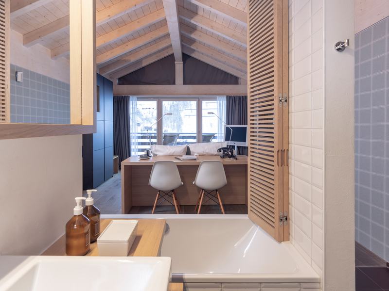 „Modernes Badezimmer mit Badewanne und Blick in ein Schlafzimmer mit Holzdecke und Arbeitsplatz