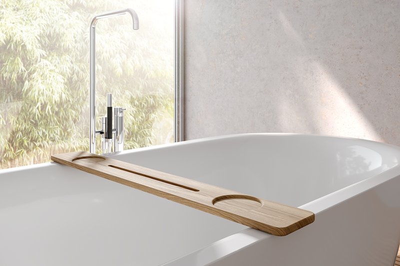 Vasca da bagno bianca freestanding con mensola da vasca in legno, rubinetteria freestanding moderna in cromo e luce naturale soffusa con vista sul verde.