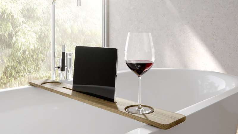 Tablet e bicchiere di vino su un ripiano in legno sopra una vasca da bagno in un bagno moderno con luce naturale.