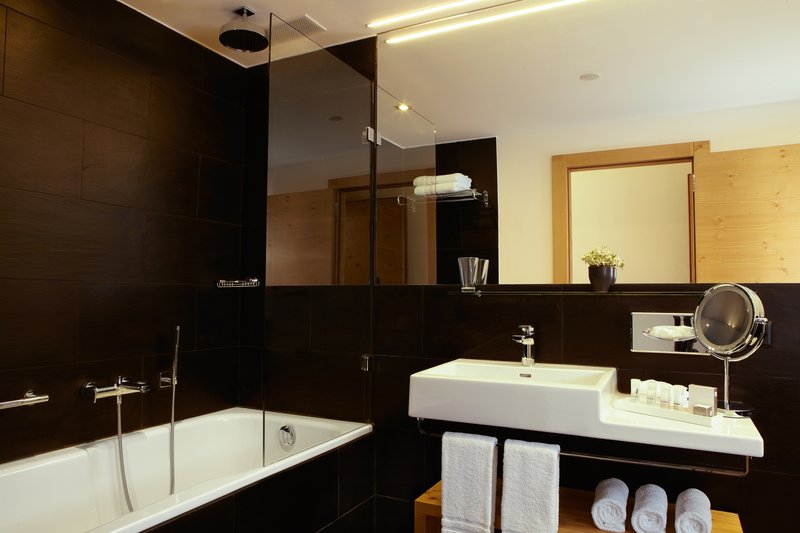 Modernes Badezimmer mit dunklen Fliesen, Badewanne, Glasduschwand und Waschtisch