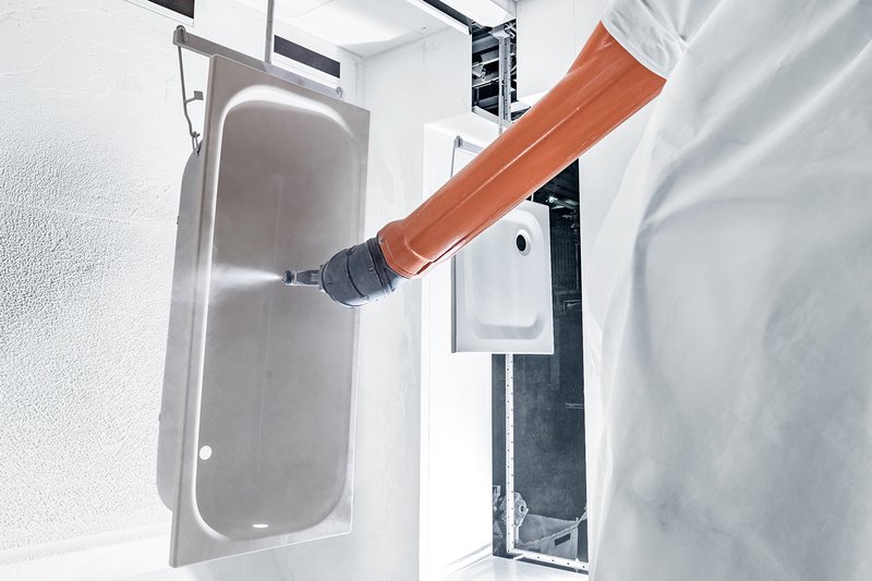 Industrieroboter besprüht eine Schmidlin Stahlbadewanne mit Email in der Produktion.