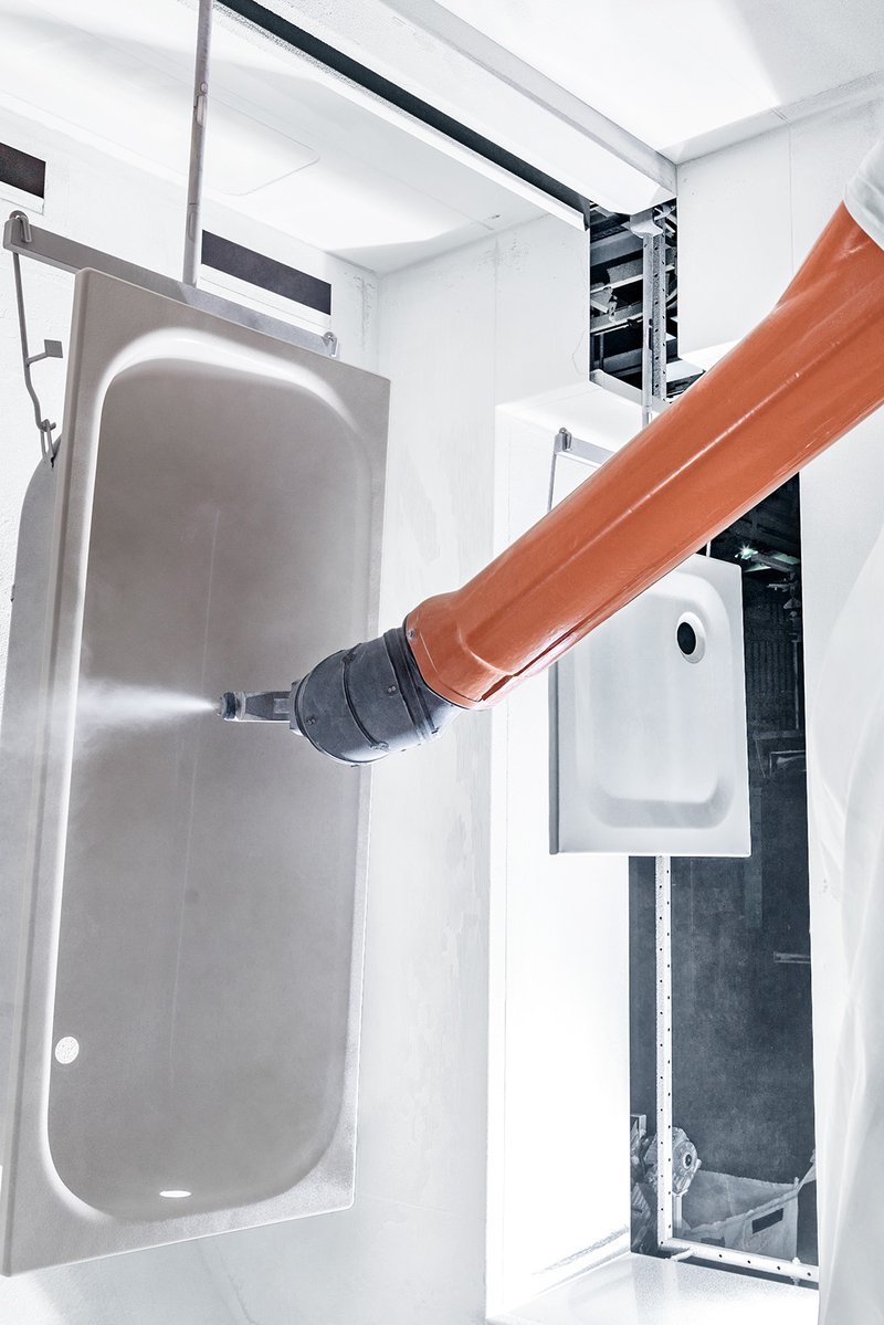 Roboter trägt Emaillebeschichtung auf eine Schmidlin Badewanne in der Produktion auf