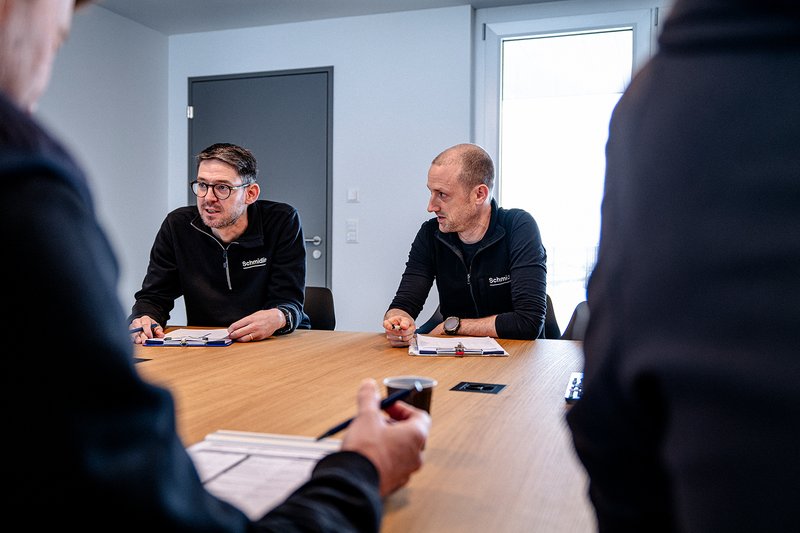 Zwei Mitarbeiter der Wilhelm Schmidlin AG diskutieren in einem Meeting am Konferenztisch mit Notizen und Unterlagen