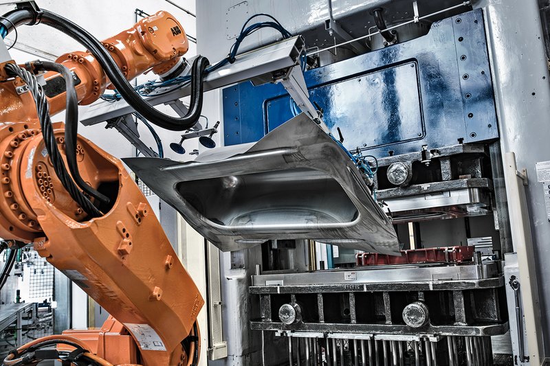 Industrieroboter entnimmt eine geformte Stahlbadewanne aus der Tiefziehpresse in der Schmidlin Produktion.