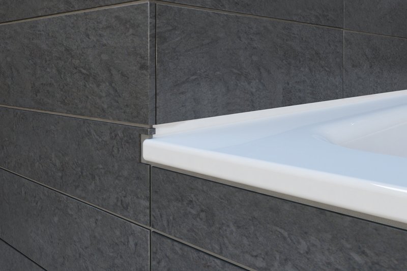 Detailaufnahme einer Schmidlin-Stahlzarge an einer Badewanne; die emaillierte Stahlkante schliesst sauber an dunkle Steinzeugplatten an, präzise eingepasst und fugenbündig in der Wandverkleidung.