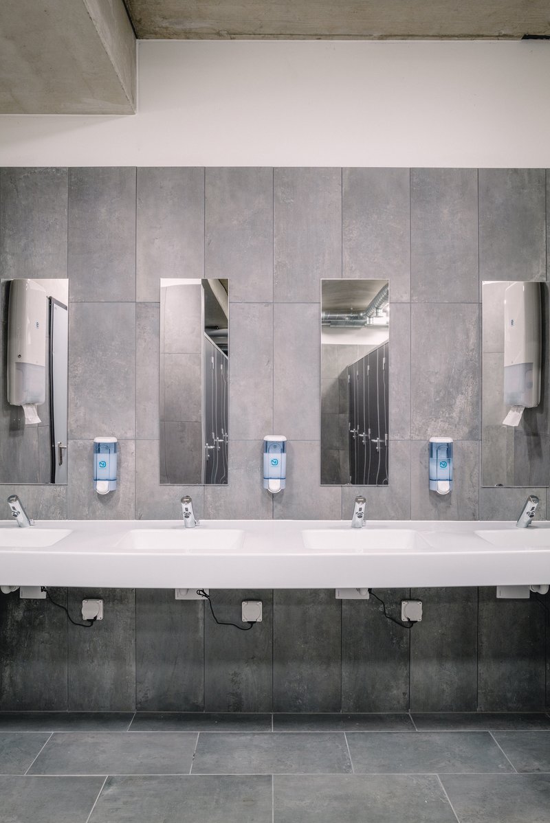 Moderner Waschraum mit mehreren Waschbecken, Spiegeln und Seifenspendern in minimalistischem Design