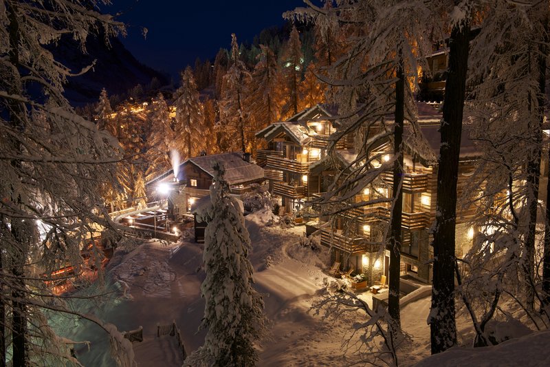 Hotel CERVO in Zermatt bei Nacht, umgeben von verschneiten Bäumen und beleuchteten Chalets