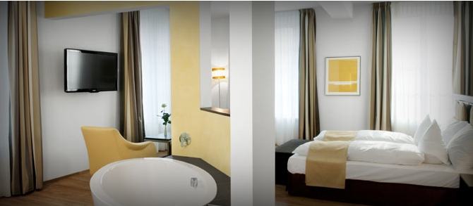 Helles Hotelzimmer mit freistehender Badewanne, Fernseher und Schlafzimmer in warmen Farbtönen