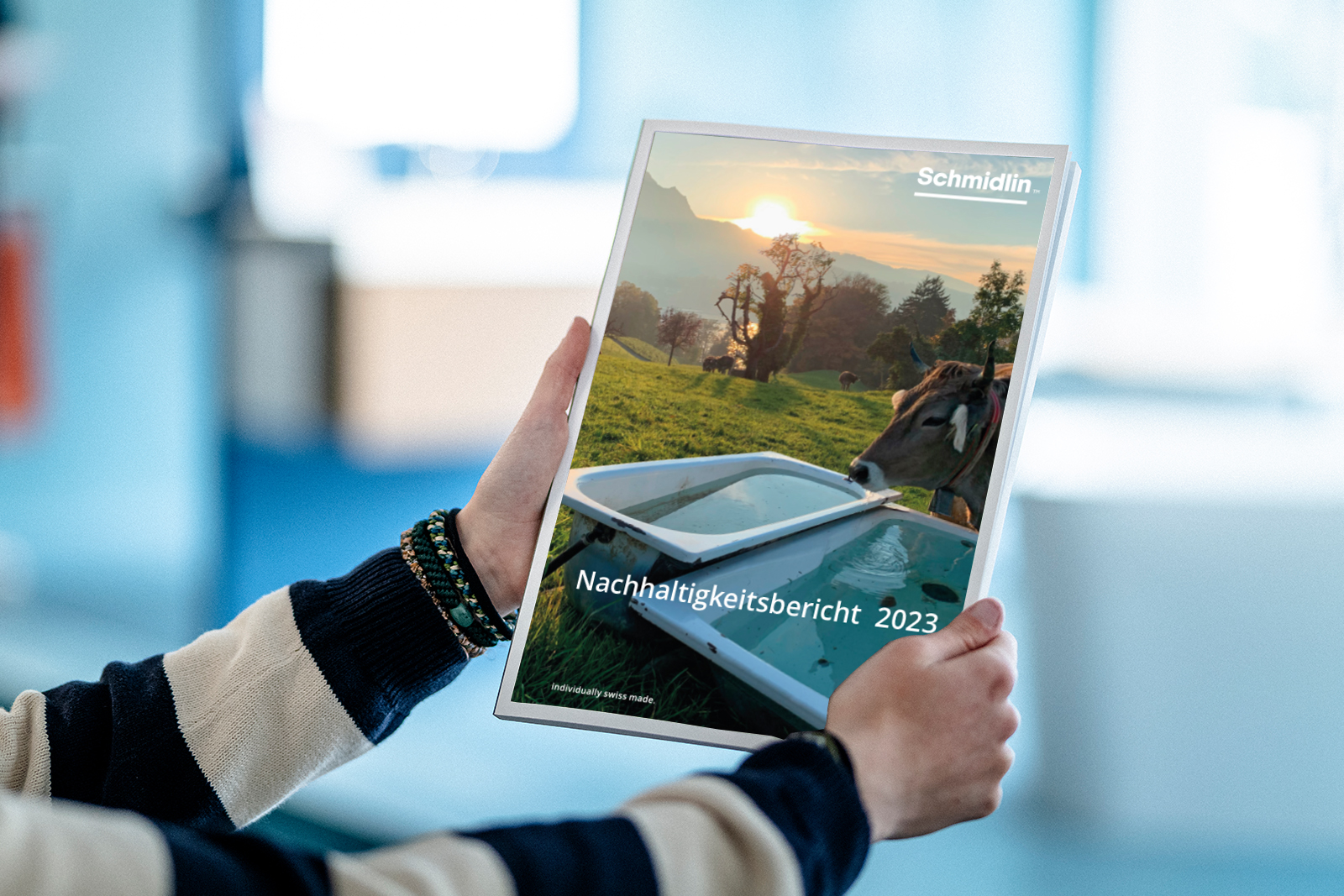 Person hält den Nachhaltigkeitsbericht der Wilhelm Schmidlin AG mit Landschaftsbild und Badewanne auf dem Cover